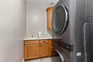 Laundry Room  with sink, stacked washing machine and dryer, cabinets, and light tile flooring