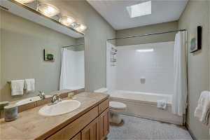 Full bathroom featuring toilet, shower / tub combo with curtain, vanity, and a skylight