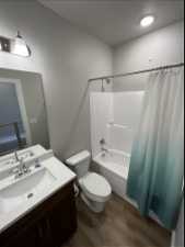 Full bathroom featuring hardwood / wood-style floors, vanity, shower / bath combo with shower curtain, and toilet