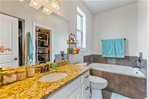 Bathroom with tiled bath, tiled separate shower, tile floors, vanity with extensive cabinet space, and toilet