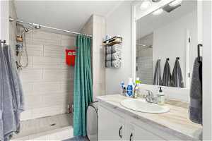 Bathroom featuring a textured ceiling, a shower with curtain, large vanity, and ornamental molding