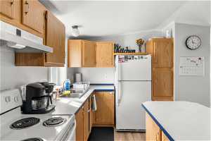 Kitchen featuring light hardwood / wood-style floors, white fridge, vaulted ceiling, stove, and ornamental molding