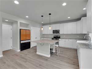 Kitchen with appliances with stainless steel finishes, light hardwood / wood-style flooring, white cabinets, a center island, and a breakfast bar area
