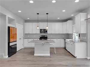 Kitchen featuring appliances with stainless steel finishes, a center island, decorative light fixtures, a kitchen breakfast bar, and light hardwood / wood-style flooring