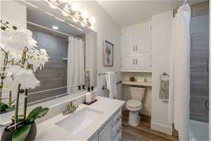 Full bathroom with shower / bath combo with shower curtain, toilet, vanity, and hardwood / wood-style flooring