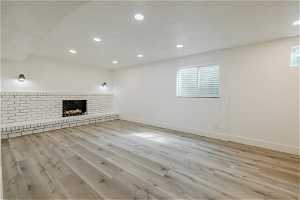 Unfurnished living room with a fireplace, brick wall, and light hardwood / wood-style flooring