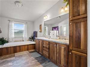 Bathroom with double sink, vanity with extensive cabinet space, a bath, a textured ceiling, and vaulted ceiling