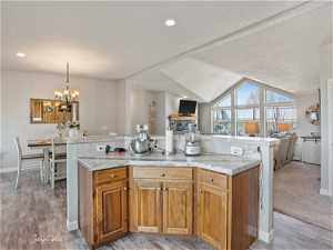 Kitchen with light colored carpet, a chandelier, light stone counters, vaulted ceiling, and pendant lighting