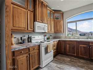 Kitchen with light stone countertops, a mountain view, dark wood-type flooring, white appliances, and sink