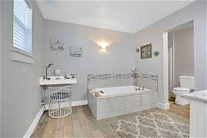 Bathroom with hardwood / wood-style flooring, toilet, vanity, and tiled tub