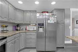 Kitchen with gray cabinets, stainless steel fridge with ice dispenser, light hardwood / wood-style flooring, light stone countertops, and tasteful backsplash