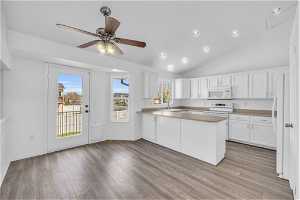 Kitchen with white cabinetry, kitchen peninsula, ceiling fan, white appliances, and vaulted ceiling