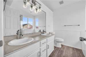 Primary Bathroom with toilet, large vanity, vaulted ceiling, hardwood / wood-style floors, and dual sinks