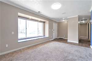 Main level living room  featuring dark carpet, ornamental molding, a textured ceiling, and baseboard heating