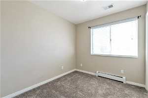 Spare room with light colored carpet and a baseboard heating unit