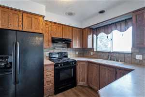 Kitchen featuring dark hardwood / wood-style floors, tasteful backsplash, sink, and black appliances