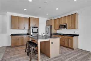 Kitchen with light hardwood / wood-style floors, a kitchen bar, an island with sink, stainless steel appliances, and sink
