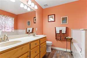 Bathroom featuring double sink, a washtub, vanity with extensive cabinet space, toilet, and hardwood / wood-style flooring