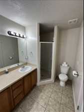 Bathroom featuring tile floors, a shower with door, large vanity, a textured ceiling, and toilet