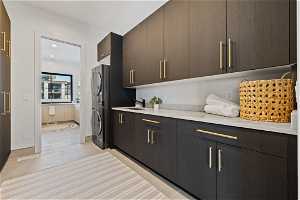 Kitchen with stainless steel refrigerator, dark brown cabinets, light tile floors, light stone countertops, and sink
