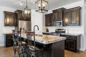 Kitchen featuring a breakfast bar, appliances with stainless steel finishes, tasteful backsplash, an island with sink, and hanging light fixtures