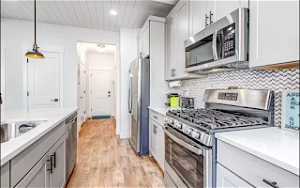 Kitchen with light hardwood / wood-style flooring, hanging light fixtures, stainless steel appliances, and tasteful backsplash