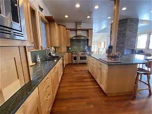 Kitchen with tasteful backsplash, dark wood-type flooring, a breakfast bar, stainless steel appliances, and wall chimney exhaust hood