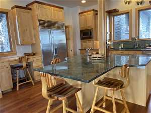 Kitchen with a center island, tasteful backsplash, a breakfast bar, dark hardwood / wood-style flooring, and built in appliances