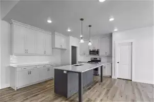 Kitchen with decorative light fixtures, appliances with stainless steel finishes, a kitchen bar, light wood-type flooring, and a center island with sink