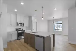 Kitchen featuring white cabinetry, light hardwood / wood-style floors, stainless steel appliances, and a kitchen island with sink