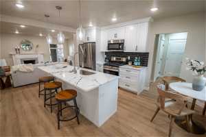 Kitchen featuring appliances with stainless steel finishes, light stone countertops, light hardwood / wood-style floors, white cabinetry, and a center island with sink