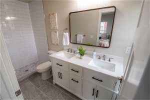 Bathroom with toilet, double sink vanity, tile flooring, and tiled shower