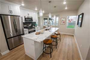 Kitchen with appliances with stainless steel finishes, white cabinets, light wood-type flooring, and a center island with sink