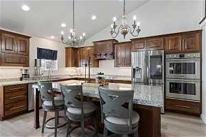 Kitchen featuring appliances with stainless steel finishes, a chandelier, a center island with sink, light hardwood / wood-style flooring, and light stone countertops