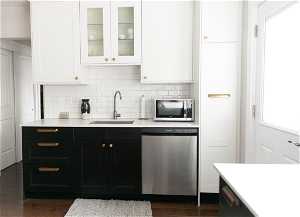 Kitchen with dark wood-type flooring, white cabinetry, stainless steel appliances, backsplash, and sink
