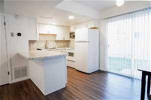 Kitchen featuring white appliances, backsplash, kitchen peninsula, dark hardwood / wood-style floors, and white cabinets