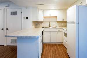Kitchen with white appliances, tasteful backsplash, dark wood-type flooring, and white cabinetry