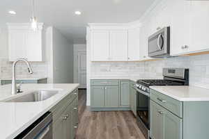 Kitchen with light wood-type flooring, pendant lighting, tasteful backsplash, white cabinets, and appliances with stainless steel finishes