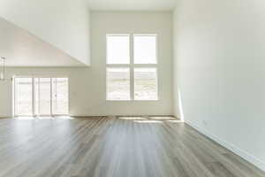 Empty room with a towering ceiling, wood-type flooring, and a notable chandelier