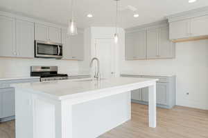 Kitchen featuring appliances with stainless steel finishes, sink, an island with sink, light wood-type flooring, and pendant lighting