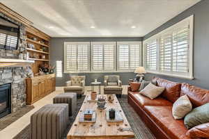 Living room with built in features, a textured ceiling, and a stone fireplace