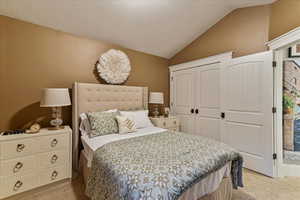 Bedroom with light colored carpet, vaulted ceiling, and a textured ceiling