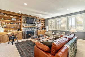 Living room with light carpet, a textured ceiling, a stone fireplace, and built in shelves