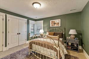 Carpeted bedroom featuring a textured ceiling and a closet