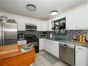 Kitchen with light tile floors, stainless steel appliances, white cabinets, backsplash, and sink
