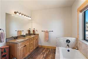 Bathroom featuring LVP floors, double sink, vanity with extensive cabinet space, and a washtub