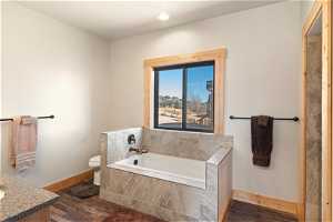 Bathroom featuring toilet, LVP flooring, vanity, and tiled tub