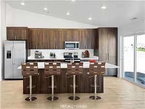 Kitchen featuring appliances with stainless steel finishes, dark brown cabinetry, a kitchen island with sink, a kitchen breakfast bar, and vaulted ceiling