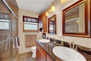Bathroom with toilet, dual sinks, large vanity, tile flooring, and an enclosed shower