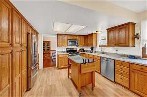 Kitchen with a breakfast bar, a kitchen island, stainless steel appliances, light wood-type flooring, and sink